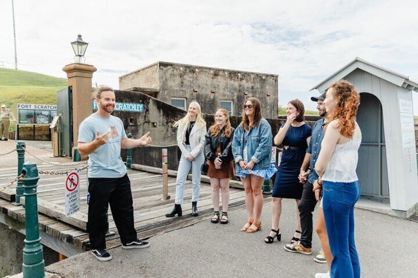 A group of people standing on a dock near a lighthouse and a building labeled 'Fort Scratchley'. 1