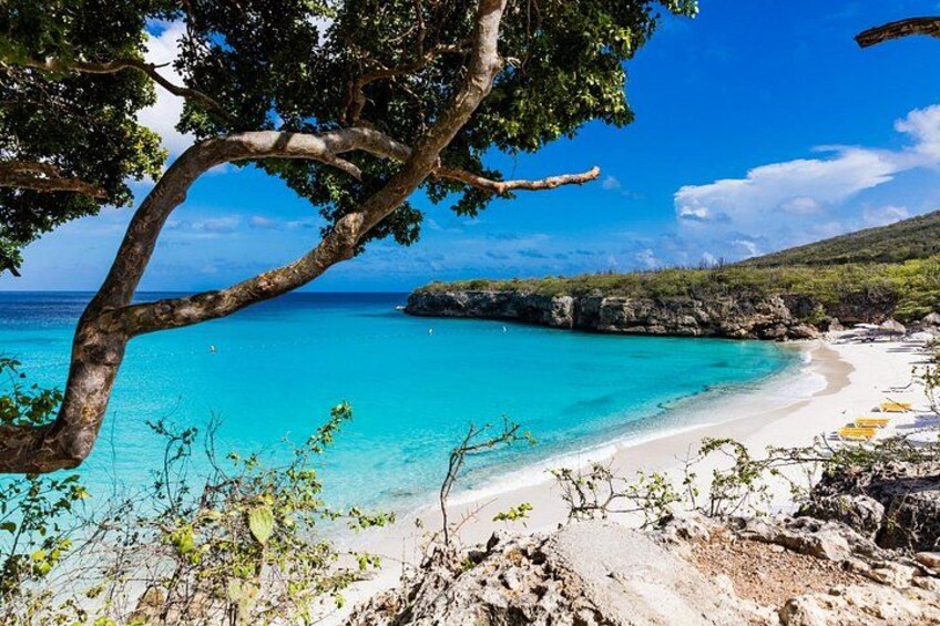 A beach with clear turquoise water, white sand, and rocky outcrops. 4