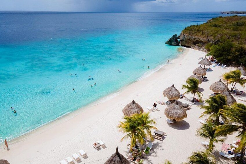 A beach with clear turquoise water, white sand, and thatched umbrellas. 2