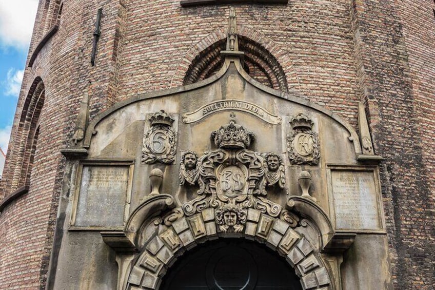 Een bakstenen toren met een stenen ingang, versierd met een familiewapen en heraldieke symbolen. 4