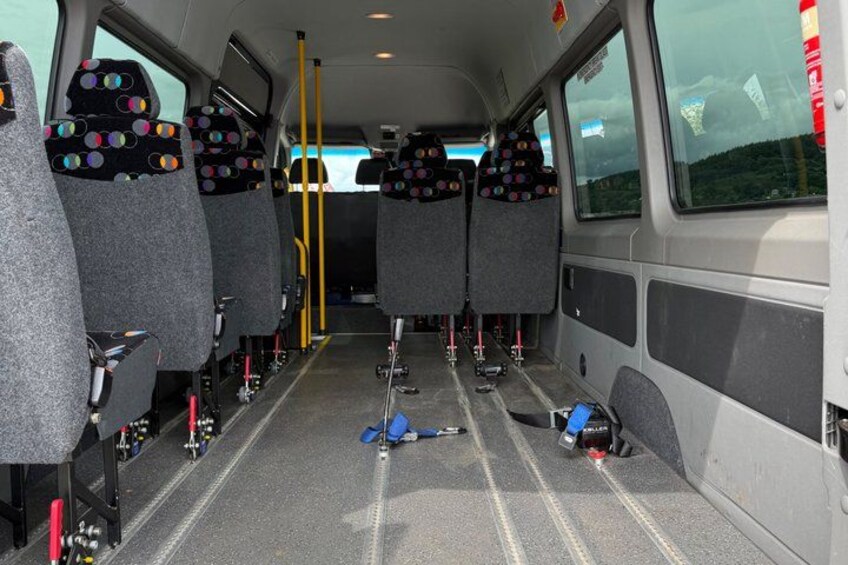 The interior of a bus with grey seats, a yellow pole, and a blue object on the floor. 5