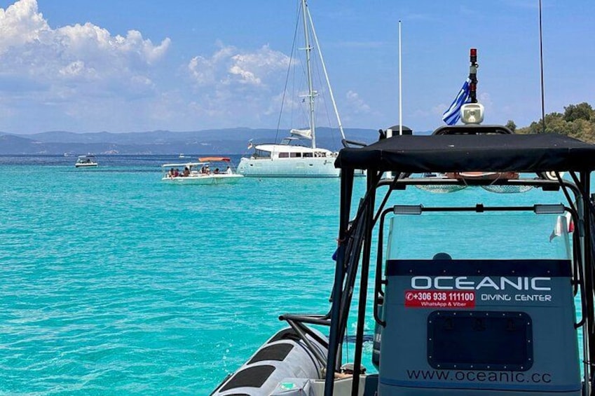 A boat with a logo and website, calm turquoise water, and sailboats in the distance. 1
