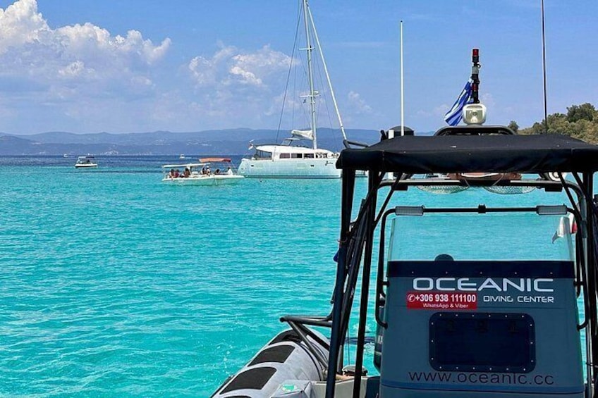 En båd med teksten 'OCEANIC DIVING CENTER', omgivet af turkis vand og andre både i baggrunden. 1