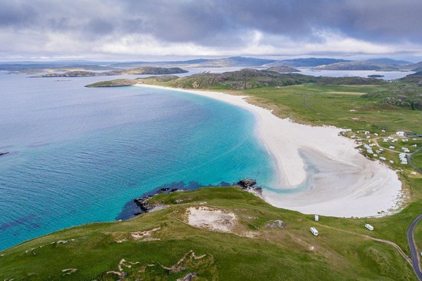 A coastal landscape with a beach, grassy areas, and a road. 1