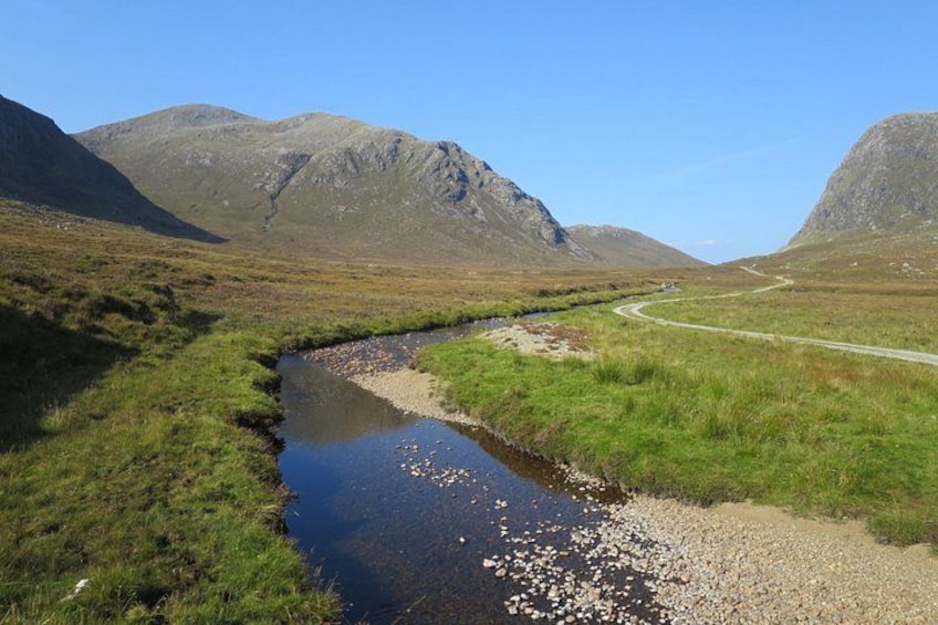 A stream, grassy fields, and mountains. 4