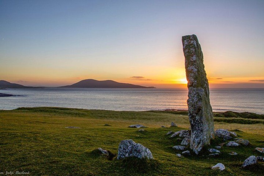 A standing stone in a grassy field with a sunset in the background. 3