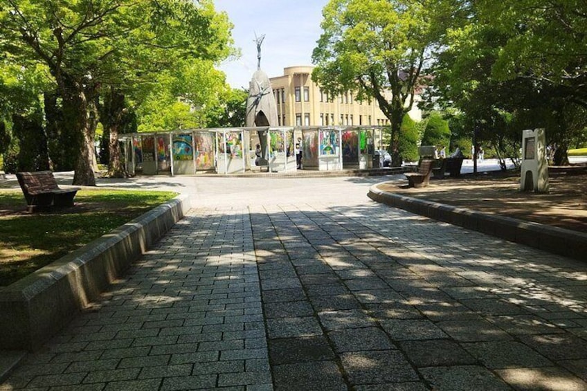A paved plaza with benches, trees, and a building with a statue in the background. 1
