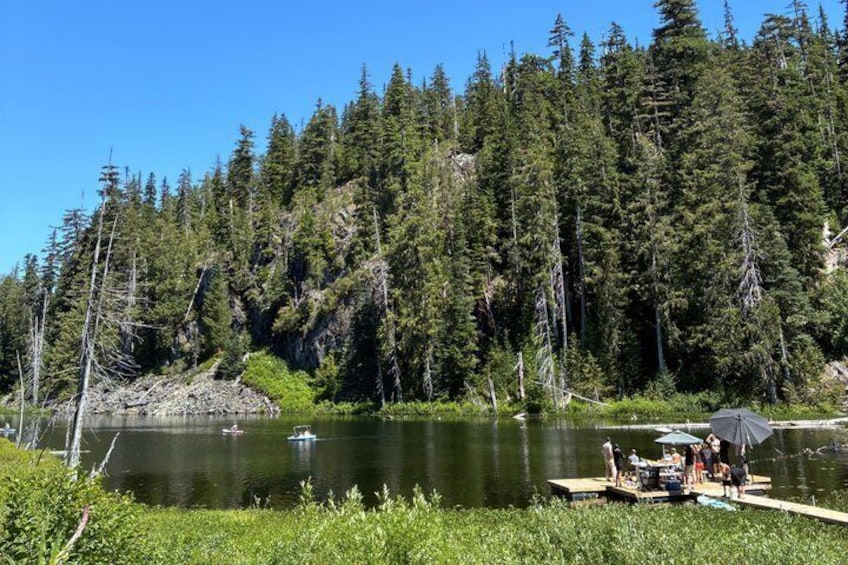 Un lago rodeado de bosque denso, un muelle con gente y un bote pequeño. 1