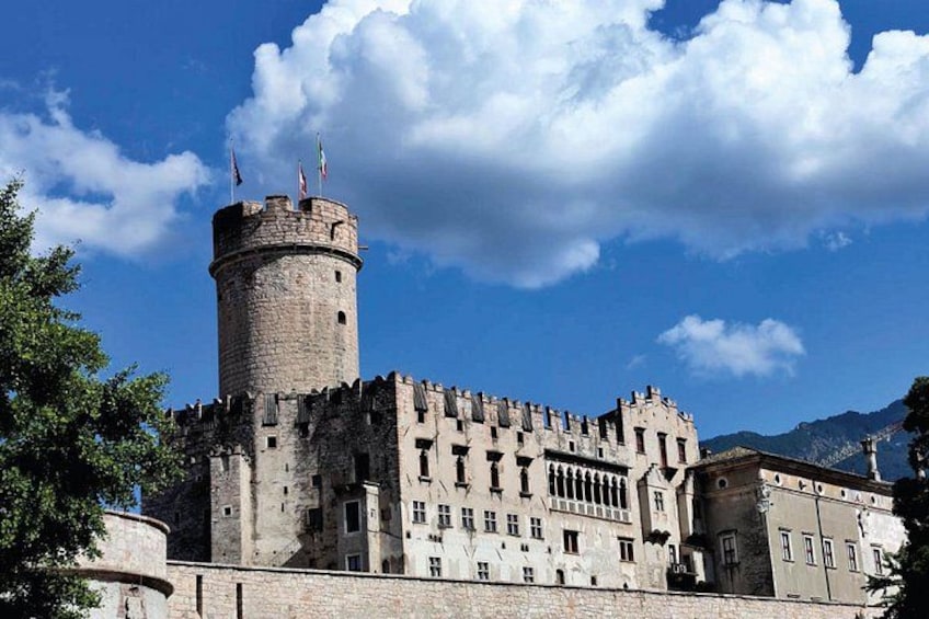 A historic stone castle with a prominent tower, surrounded by trees and under a clear blue sky. 1