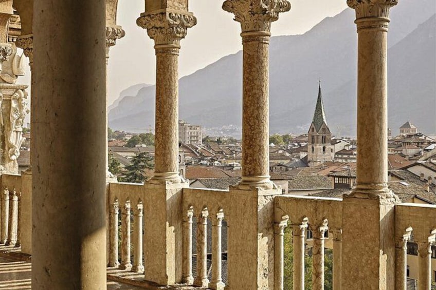 A historical building with ornate columns and a view of a town with a church spire in the background. 3