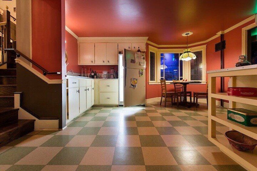 A kitchen with a checkered floor, white cabinets, a dining table, and a staircase. 1