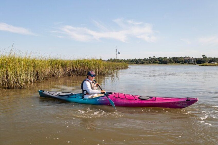 A person kayaking on a calm river with tall grasses and a clear sky. 3