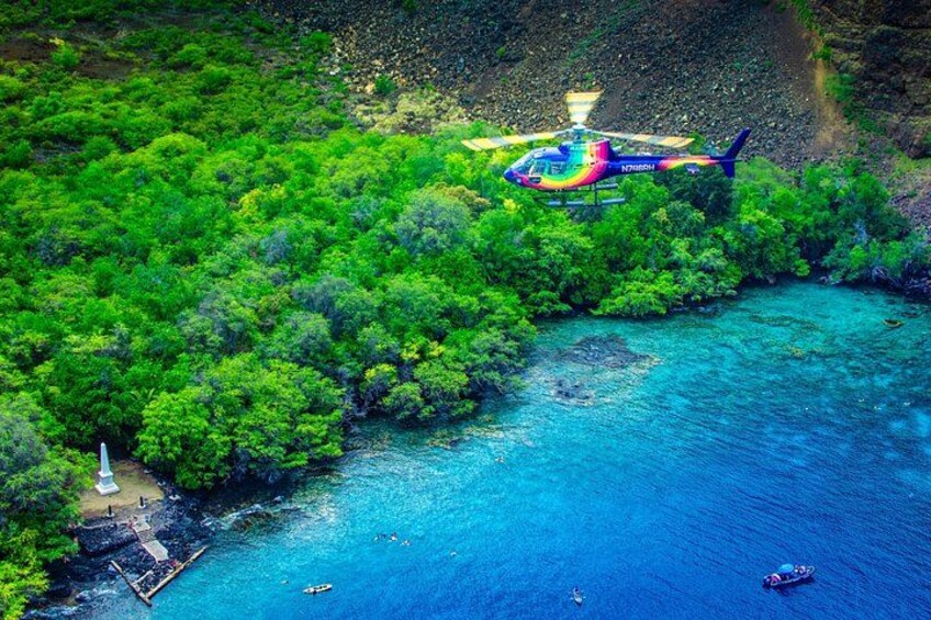 A helicopter over a lush green area with a clear blue sea, a small dock, and a white structure. 4