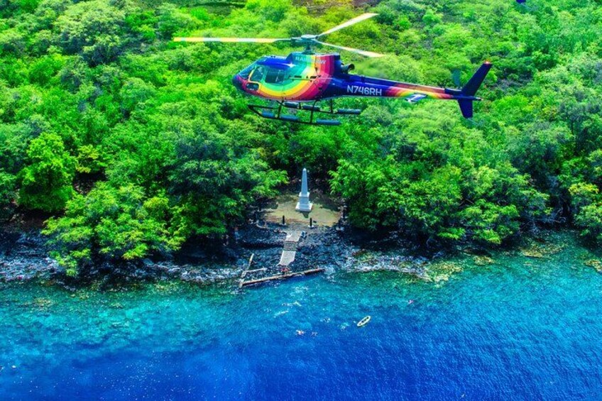 A helicopter flying over a lush green island with a dock and a small boat. 1
