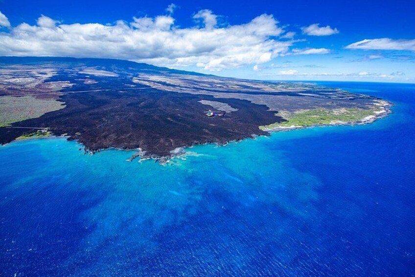 An aerial view of a coastal landscape with clear blue waters, a dark forested area, and a distant shoreline. 3