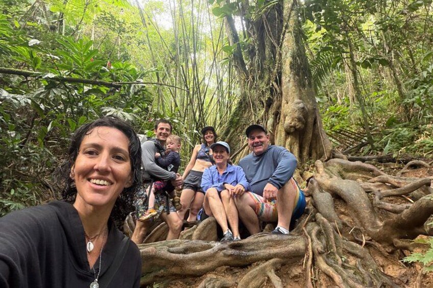 A group of people sitting on a tree root in a forest. 2