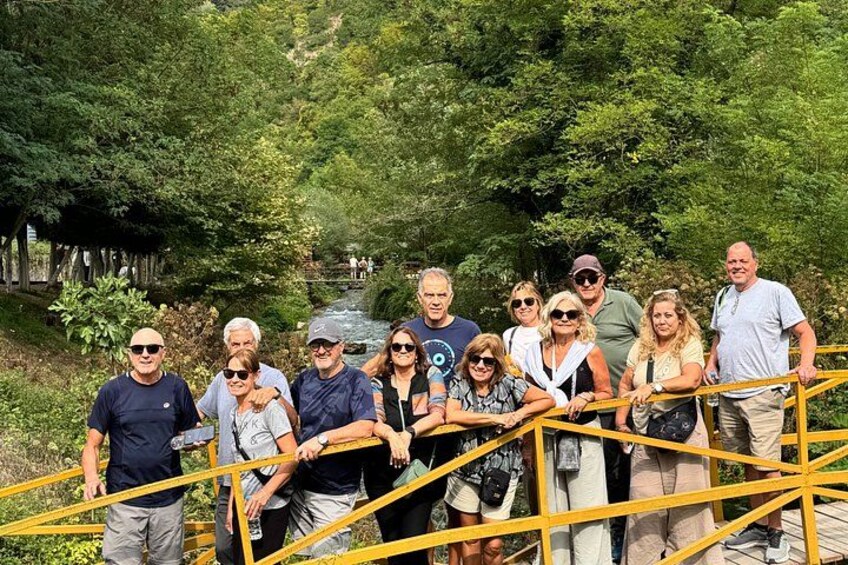A group of people standing on a bridge with a river and greenery in the background. 2