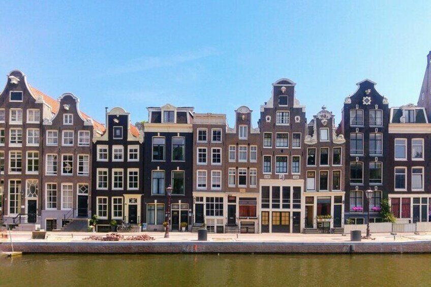 A row of historic buildings with gabled roofs and large windows along a canal. 3