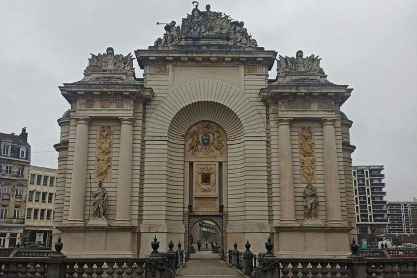 A grand, ornate archway with statues and intricate carvings, surrounded by a fence and buildings. 4