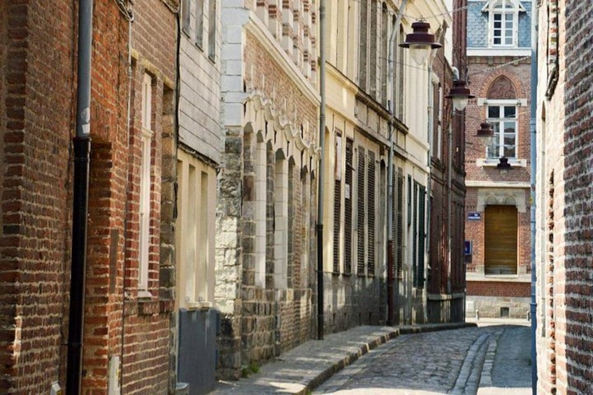 A narrow cobblestone street flanked by historic buildings with arched windows and brick facades. 2