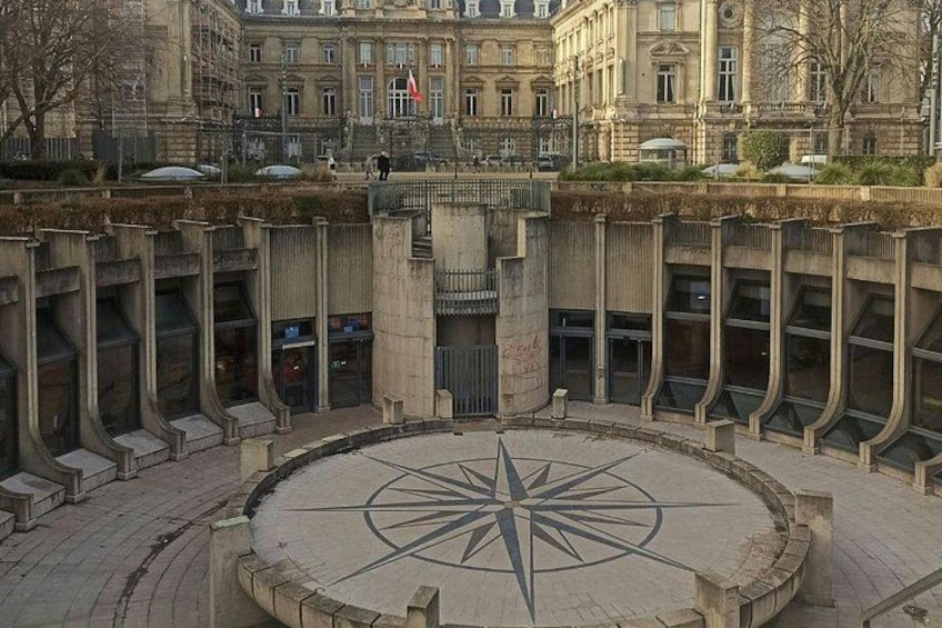 A plaza with a large compass rose in the center, surrounded by buildings with classical architecture. 1