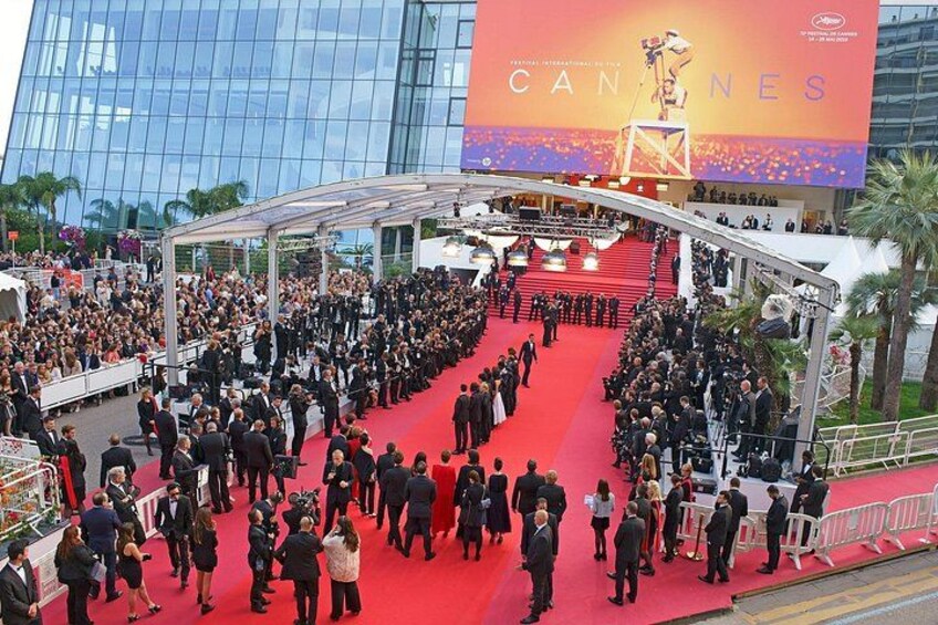 Evento sul tappeto rosso durante il Festival di Cannes, con una folla numerosa e un edificio importante sullo sfondo. 1