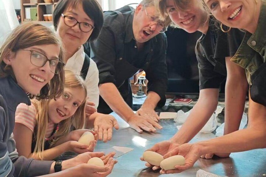 A group of people engaged in a hands-on activity, possibly a workshop or class, with objects that resemble eggs on a table. 5
