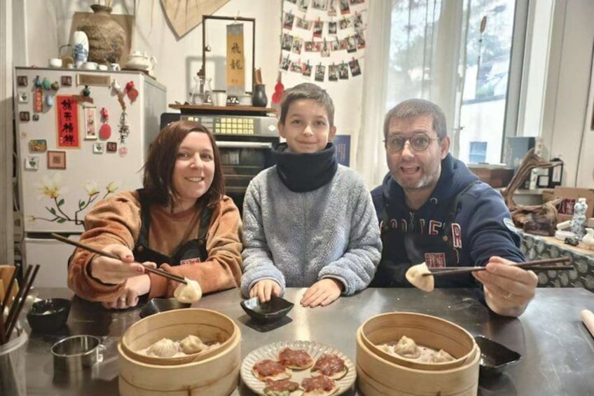 Three people sitting at a table with food, a kitchen counter, and various kitchen items in the background. 4