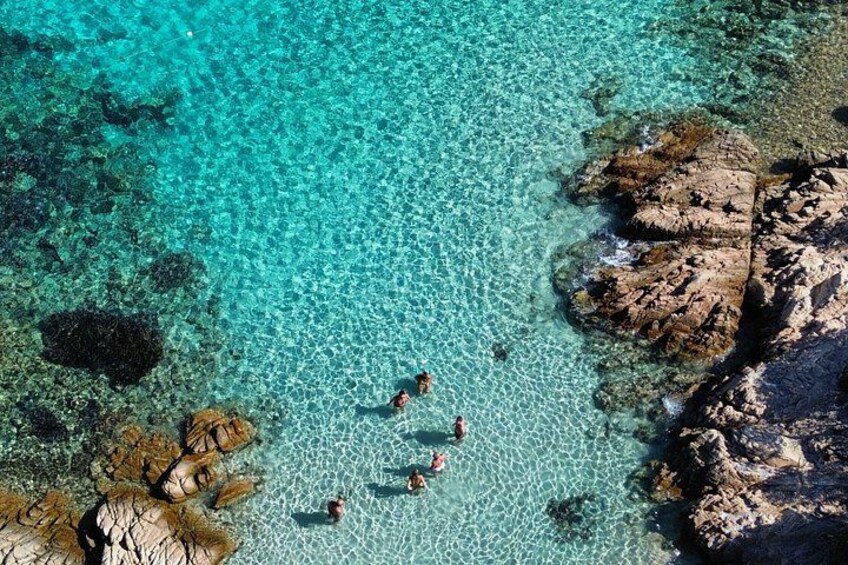 A clear turquoise sea with rocky formations and people swimming. 2