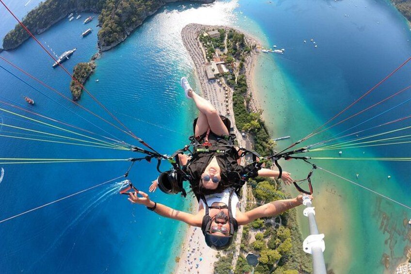 Una persona practicando parapente sobre una zona costera con aguas azules cristalinas, una playa y barcos. 3