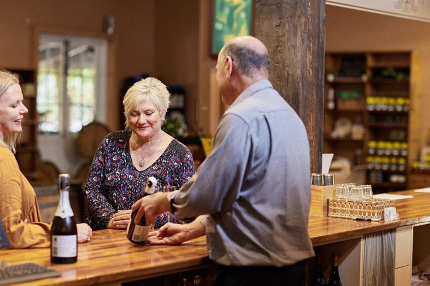 A bar setting with a wooden counter, a bottle of wine, and a person interacting with a customer. 2