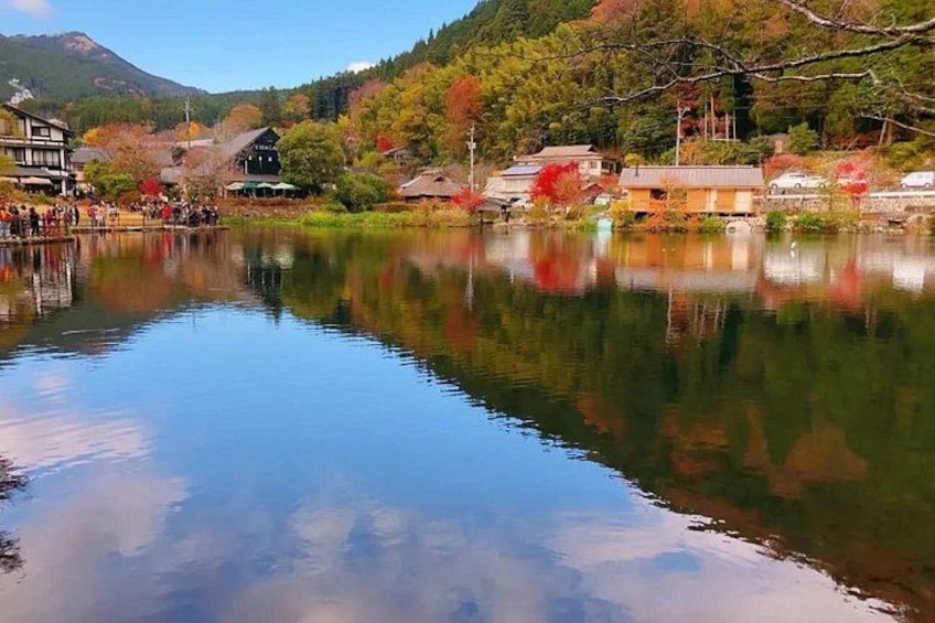 A calm lake with reflections of buildings and trees, surrounded by a mountainous landscape. 1