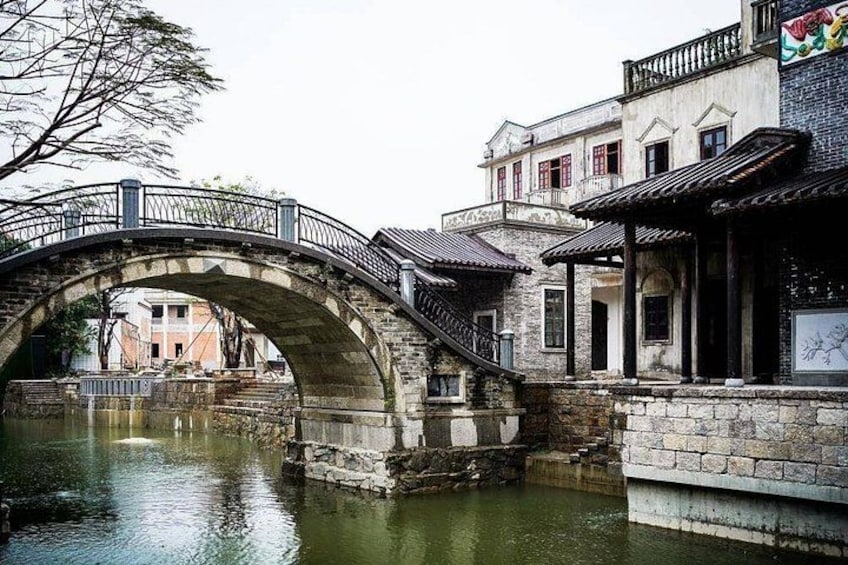 A stone bridge over a canal, traditional buildings, and a tree. 5