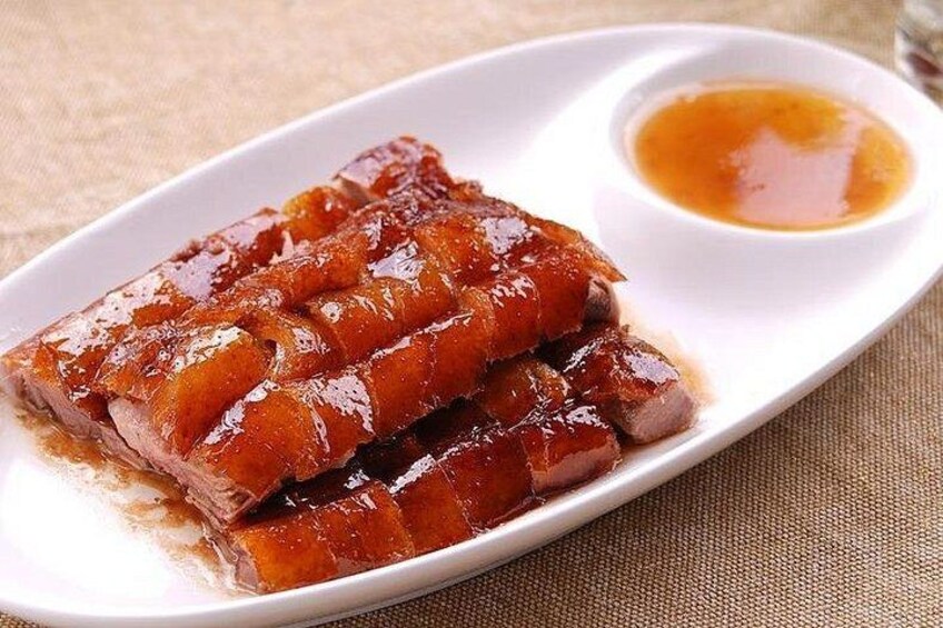 A plate of roasted duck with a glossy glaze and a small bowl of sauce. 4