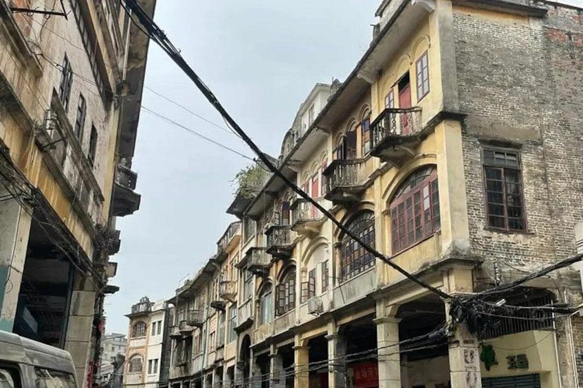 A narrow street lined with old buildings, some with balconies and visible wear. 3