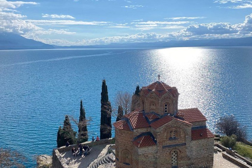 A church with a red roof, a body of water, and mountains in the background. 1