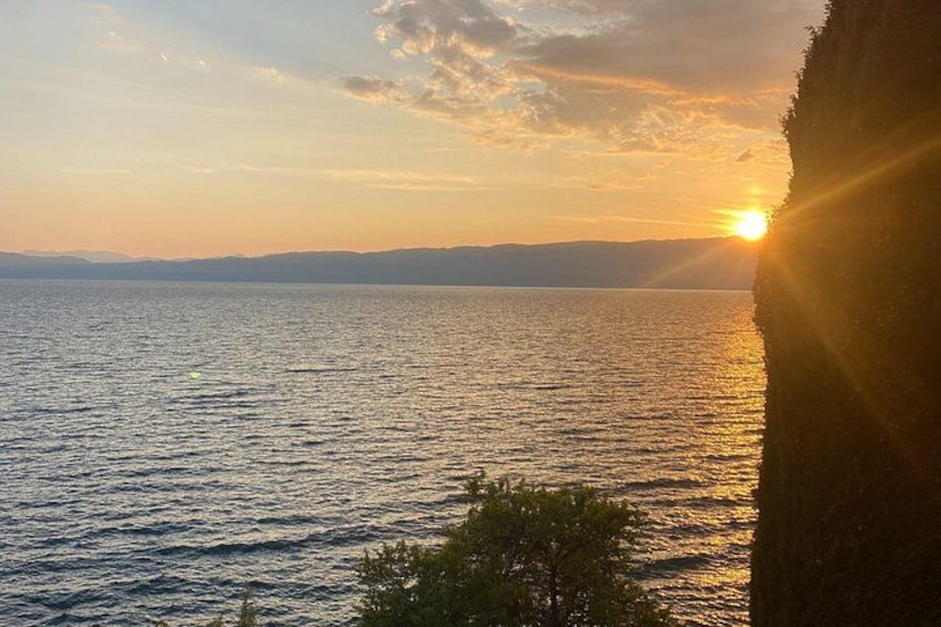 A sunset over a body of water with a silhouette of a cliff and some vegetation in the foreground. 4