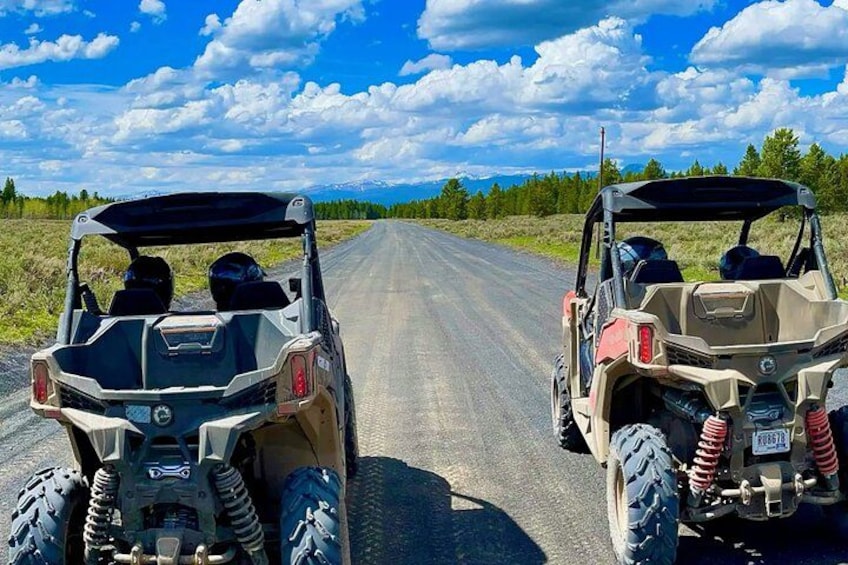 Two off-road vehicles on a paved road with a clear sky and distant mountains. 1