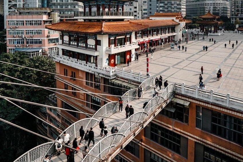 A pedestrian bridge with people walking, a traditional building with a tiled roof, and a large open square. 2