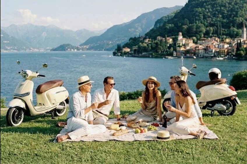 A group of people on a picnic with a lake and mountains in the background. 1