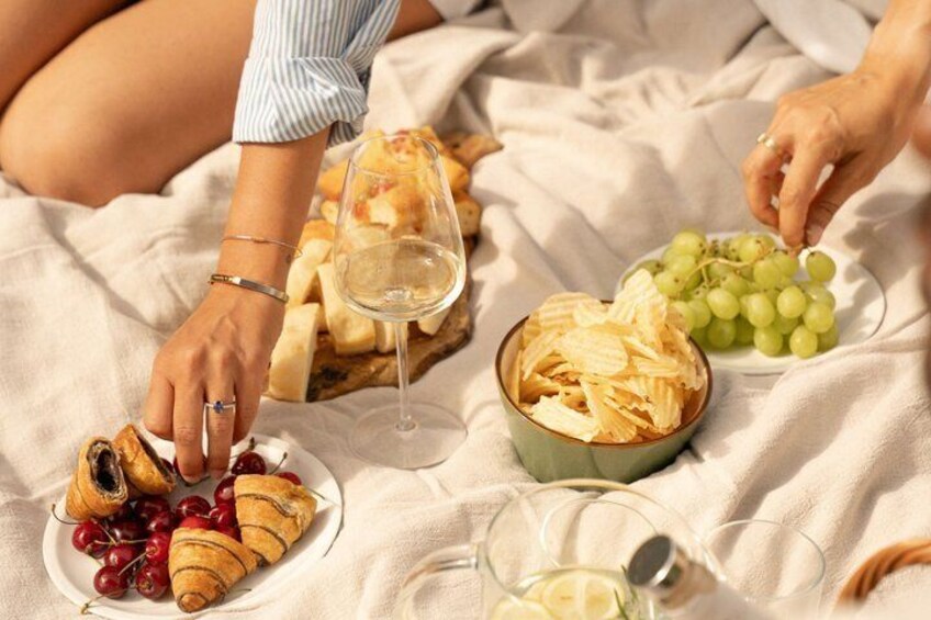 A picnic with croissants, grapes, cheese, and wine glasses on a blanket. 5