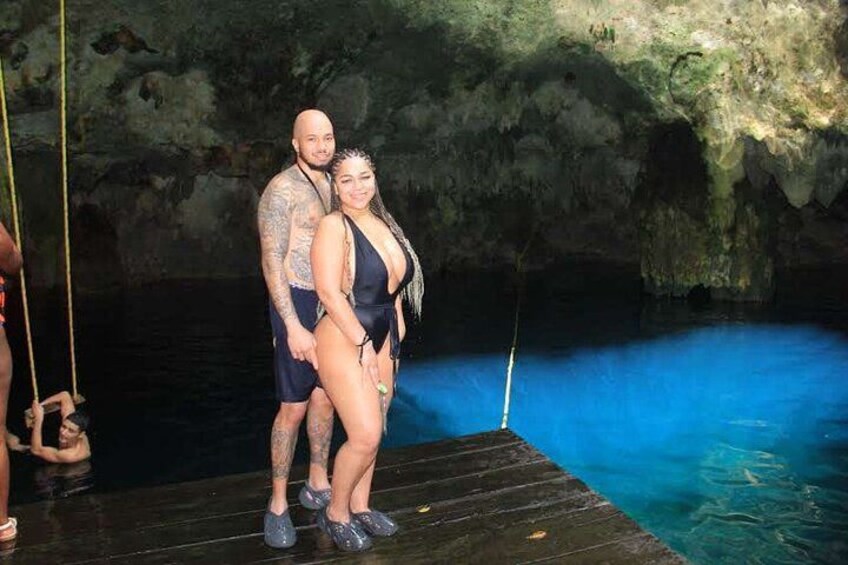 Ein Paar steht auf einem hölzernen Steg an einem blauen Pool in einer höhlenartigen Umgebung. 2