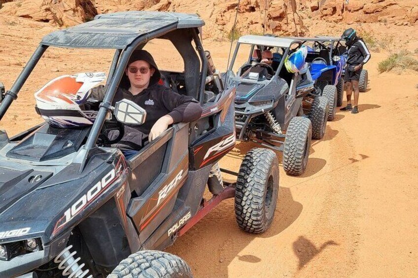 Een persoon in een Polaris 1000 RZR op een zandpad, samen met andere voertuigen voor offroad gebruik. 5