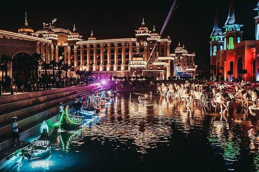 A nighttime scene with illuminated buildings, a canal with gondolas, and a crowd of people. 4