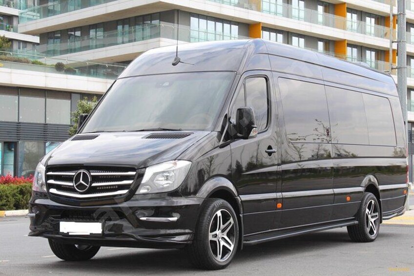 A black Mercedes van parked in front of a modern building with large windows and balconies. 3