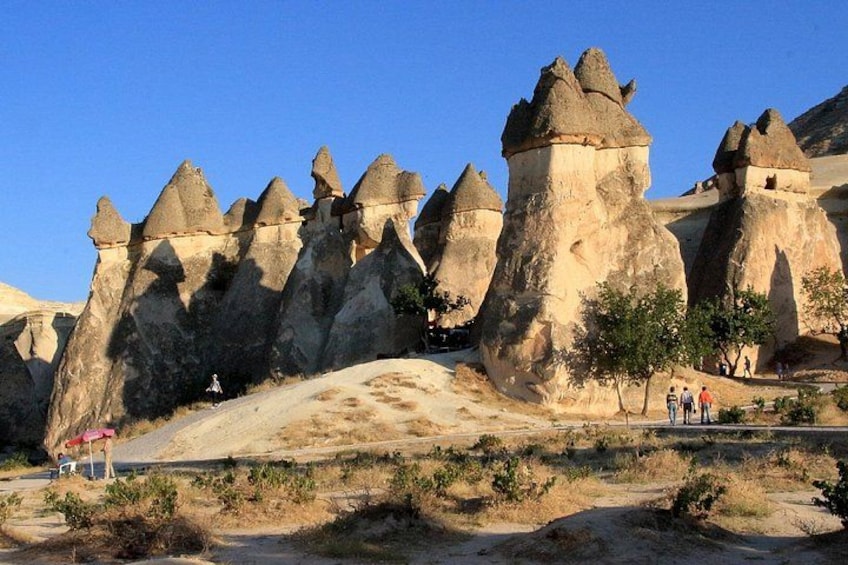 A landscape with unique rock formations, a clear sky, and a few people walking. 4