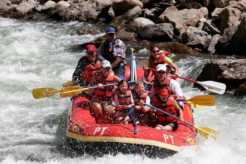 A group of people in a red raft navigating a river with rapids. 1