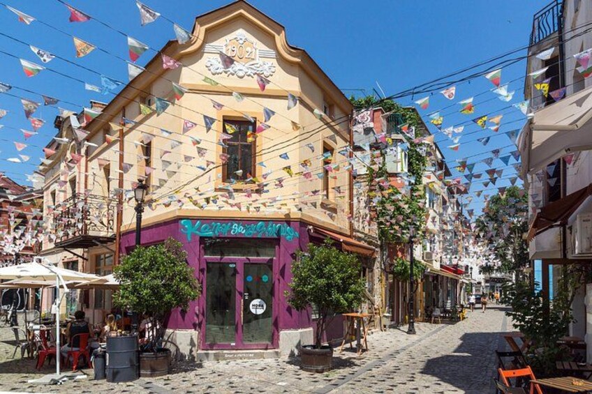 A street with buildings, a shop with a purple awning, and colorful triangular flags. 2