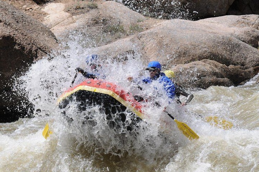 A white kayak with a red and yellow design navigating through a river with rapids. 3