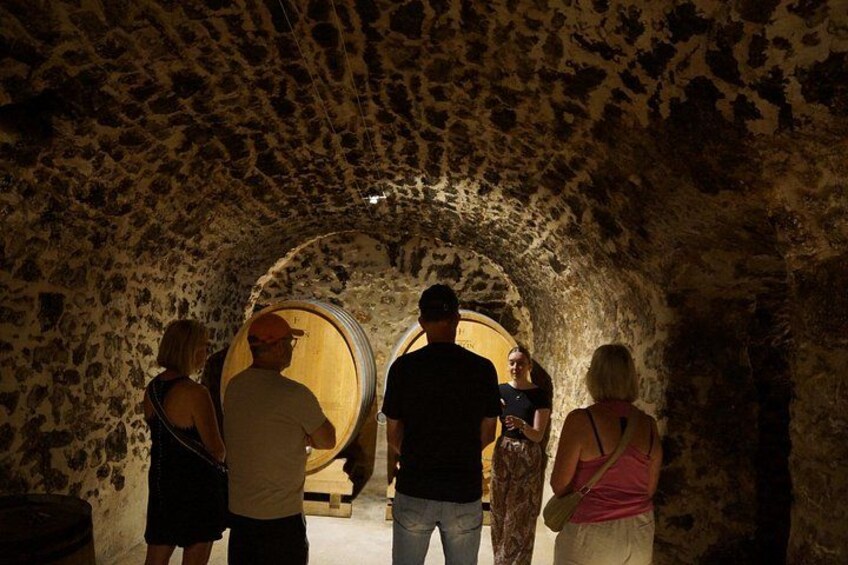 A group of people inside a stone-walled tunnel with two large wooden barrels. 5